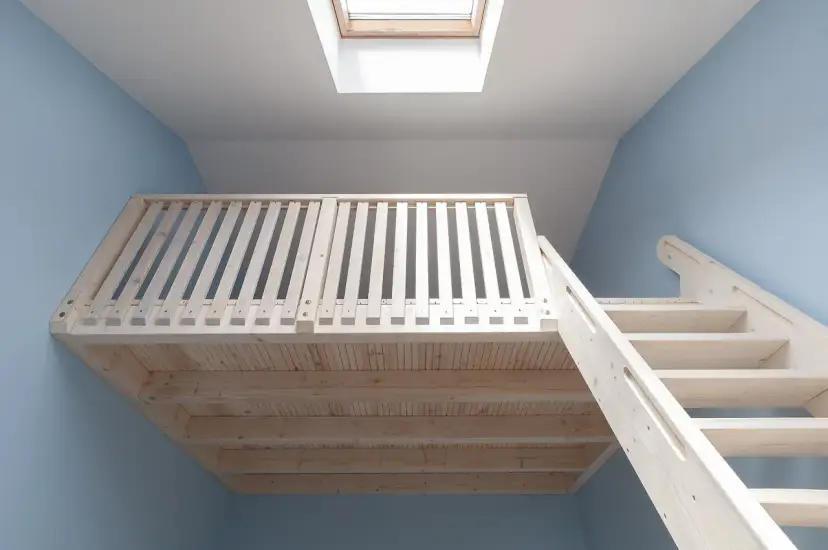 Jasna, drewniana antresola z balustradą i schodami, podświetlona przez okno dachowe.