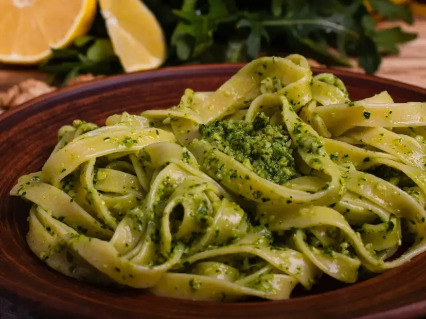 Pappardelle z aromatycznym makaronem z pesto, podane na glinianym talerzu. W tle cytryny i rukola.