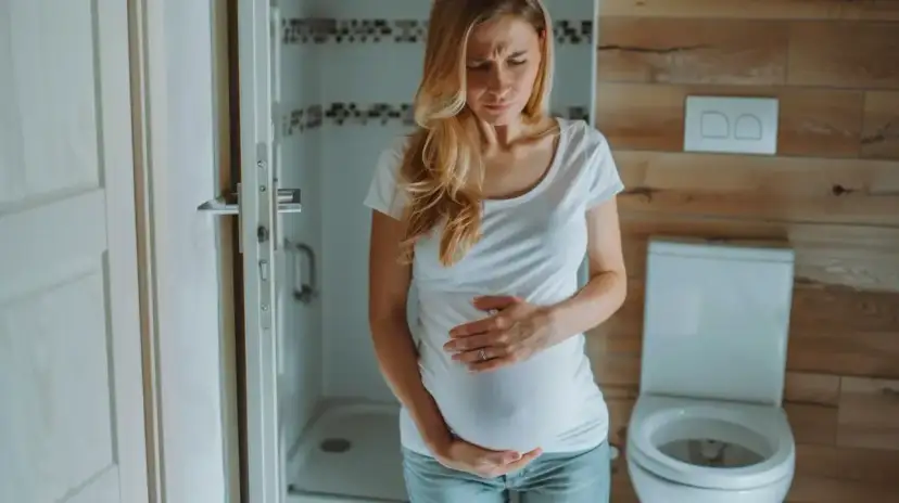 Kobieta w ciąży z bólem brzucha, która musi skorzystać z toalety. Kichanie w ciąży bywa uciążliwe.