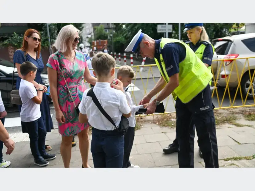 Policjant pomaga dziecku przejść przez ulicę, przypominając, od ilu lat dziecko może samo chodzić do szkoły.
