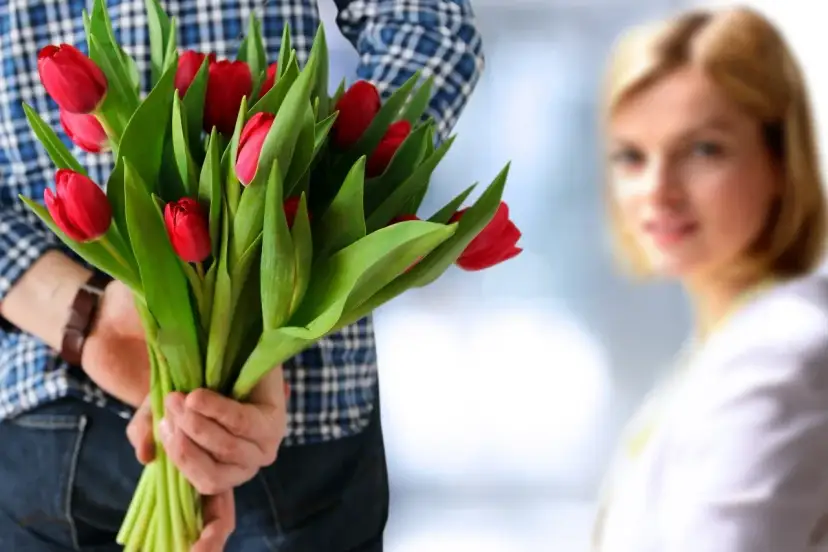 Mężczyzna z bukietem czerwonych tulipanów za plecami, zbliża się do kobiety.