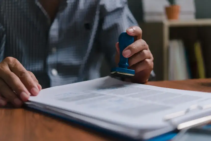 Dłoń z pieczątką nad dokumentem.