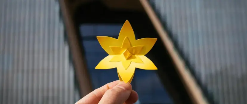 Żółty, papierowy żonkil, symbolizujący nadzieję i nowy początek, trzymany na tle nowoczesnego budynku.