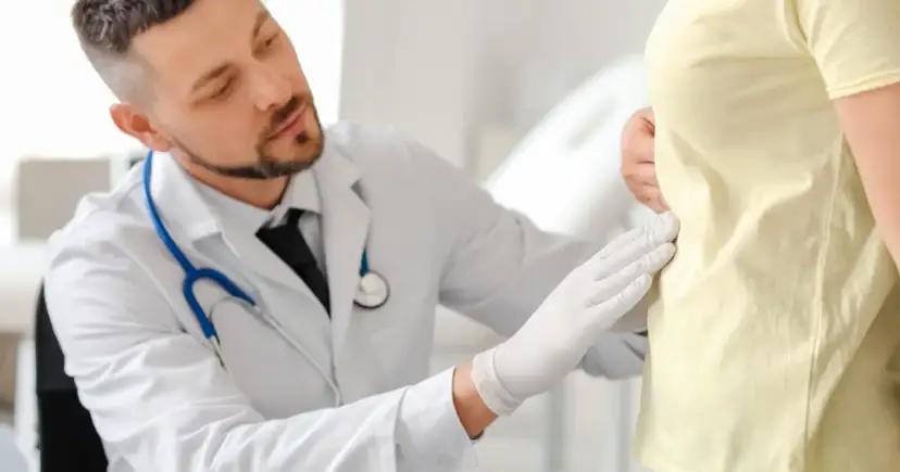 Lekarz w białym fartuchu i rękawiczkach bada pacjenta.