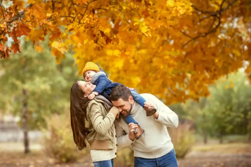 Rodzina ciesząca się jesiennym spacerem pod drzewem w złotych liściach.