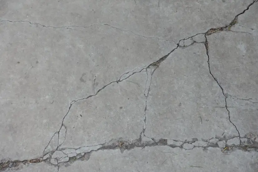 Popękany beton, jakby po długim okresie podlewania, z widocznymi szczelinami i drobnymi źdźbłami trawy.