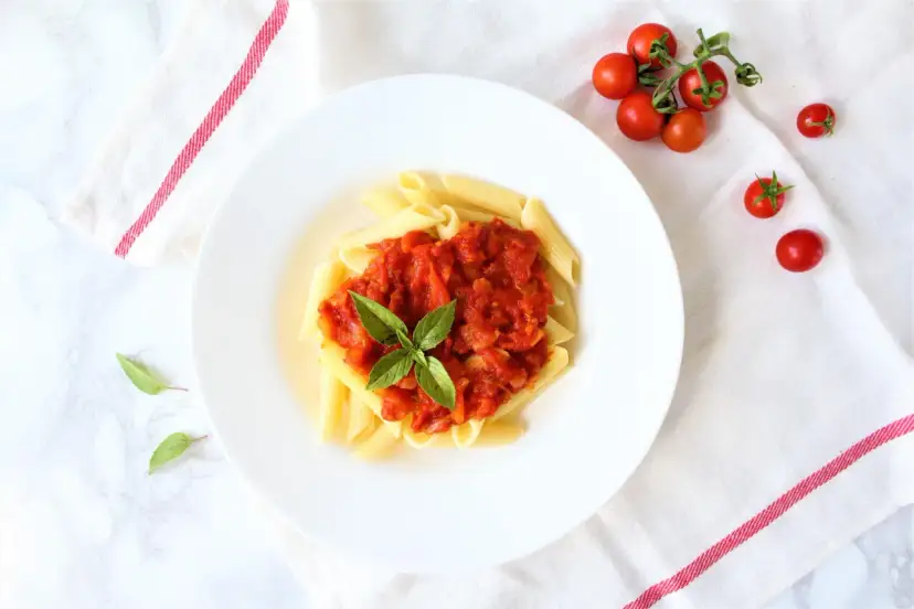 Penne z sosem pomidorowym i bazylią, obok świeże pomidorki koktajlowe.