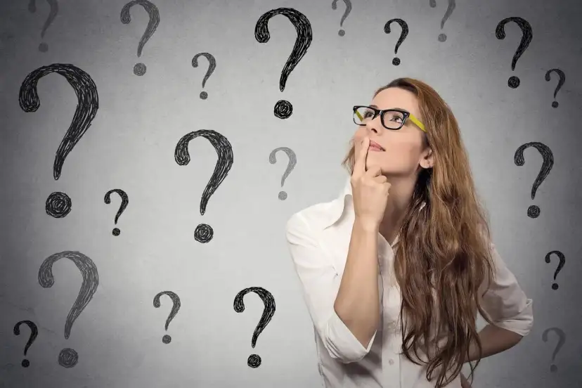 Kobieta w okularach z palcem przy ustach, otoczona znakami zapytania.