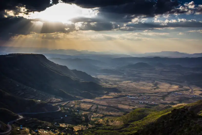 Promienie słońca przebijające się przez chmury nad malowniczymi dolinami i tarasowymi polami. Widok na wioskę i krętą drogę, ukazujący piękno etiopskich atrakcji.