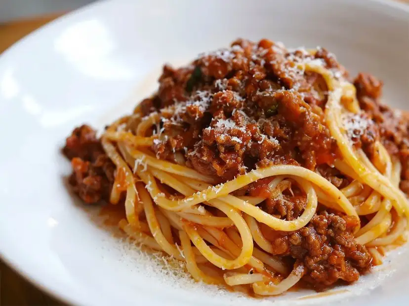 Pyszne spaghetti bolognese z bogatym sosem mięsnym i startym parmezanem na białym talerzu.