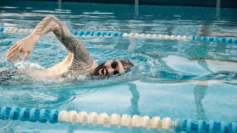 Pływak z tatuażem na ramieniu wykonuje ruch kraulem w basenie.