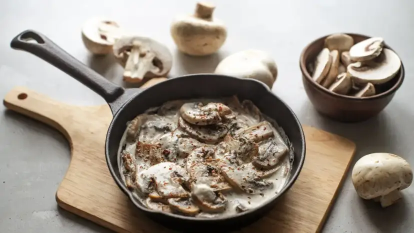 Kremowy sos pieczarkowy do makaronu w żeliwnej patelni, otoczony świeżymi pieczarkami.