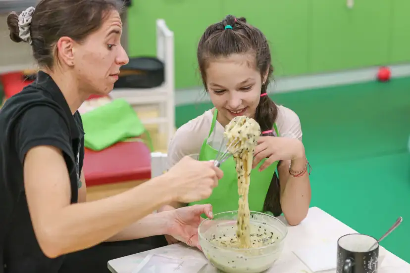 Dziecko z uśmiechem miesza masę, a terapeutka wspiera je w ćwiczeniach ręki.