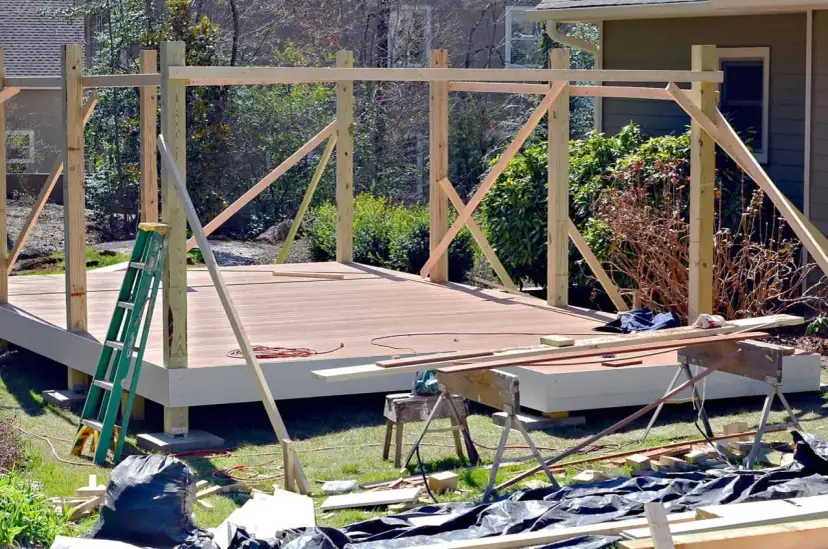 Drewniana konstrukcja altany w trakcie budowy, z widocznym stelażem pod dach i deskami tarasowymi.