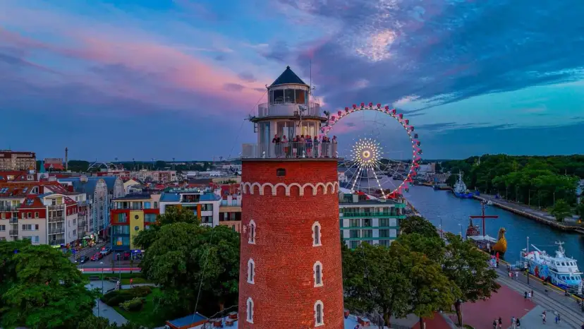 Widok na latarnię morską, diabelski młyn i port w Kołobrzegu o zachodzie słońca.