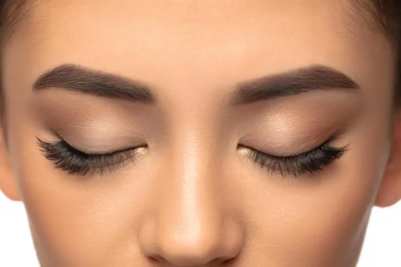 Zbliżenie na oczy kobiety z makijażem i doczepionymi kępkami rzęs.