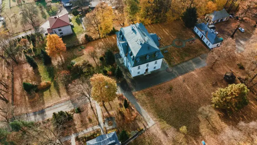 Widok z lotu ptaka na wieś z budynkami i jesiennymi drzewami pokrytymi liśćmi.