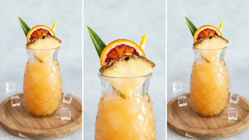 Orzeźwiający drink z ananasem i pomarańczą w szklance w kształcie ananasa, ozdobiony owocami i słomką.