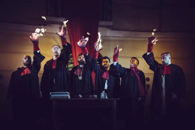 Mężczyźni w togach z płonącymi dłońmi, jakby odtwarzali legendę o czarciej łapie.