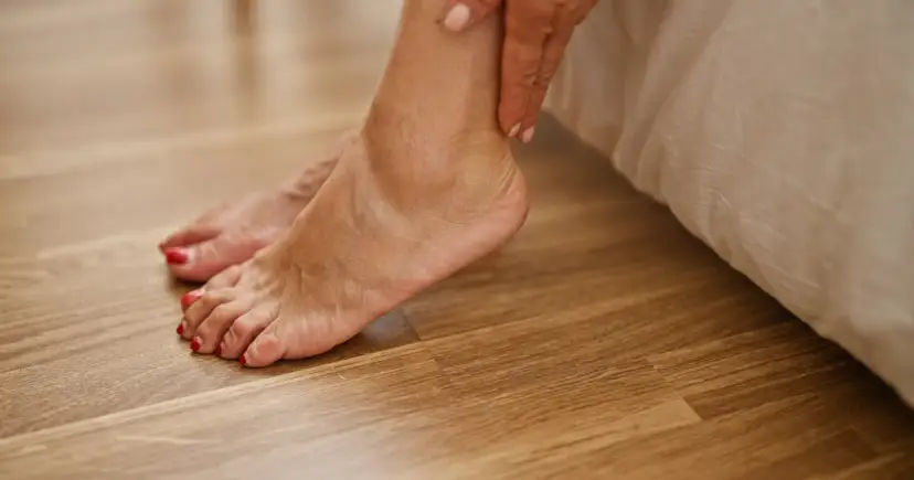 Dłoń dotyka kostki, a czerwone paznokcie stóp błyszczą na drewnianej podłodze. Ciekawe, ile centymetrów ma stopa?