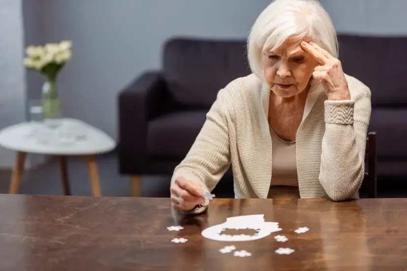Starsza kobieta zmagająca się z układanką, symbolizującą wczesny alzheimer. Jej zamyślona twarz i gest wskazują na trudności z pamięcią.