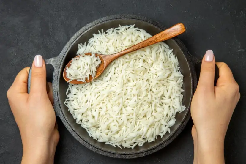 Sypki ryż basmati w misce, nabierany drewnianą łyżką, trzymany przez dwie dłonie.