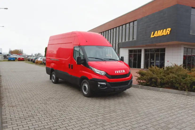 Czerwony bus Iveco na parkingu przed budynkiem z napisem LAMAR.