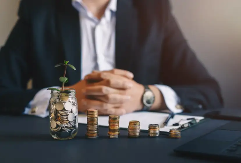 Słoik z monetami i roślinką, stosy monet i biznesmen w garniturze. Klucz do tego, jak znaleźć inwestora do biznesu.