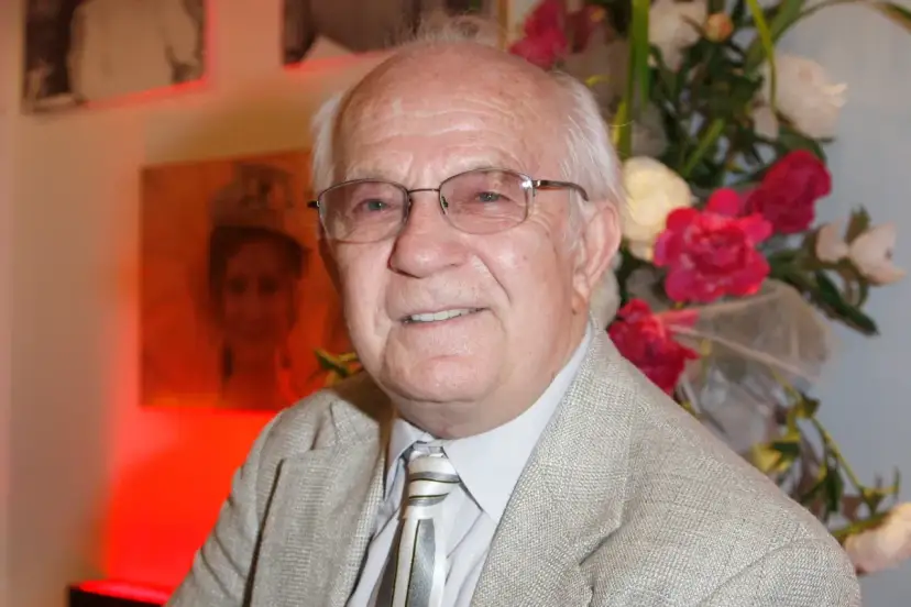 Uśmiechnięty Jerzy Antczak, reżyser znany z niezapomnianych filmów, w eleganckim garniturze, na tle bukietu kwiatów i portretu.