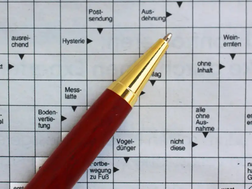 Ein roter Stift liegt auf einem Kreuzworträtsel mit deutschen Begriffen.