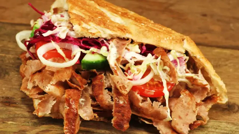 Kebab z mięsem, warzywami i sosem w bułce na drewnianym tle.