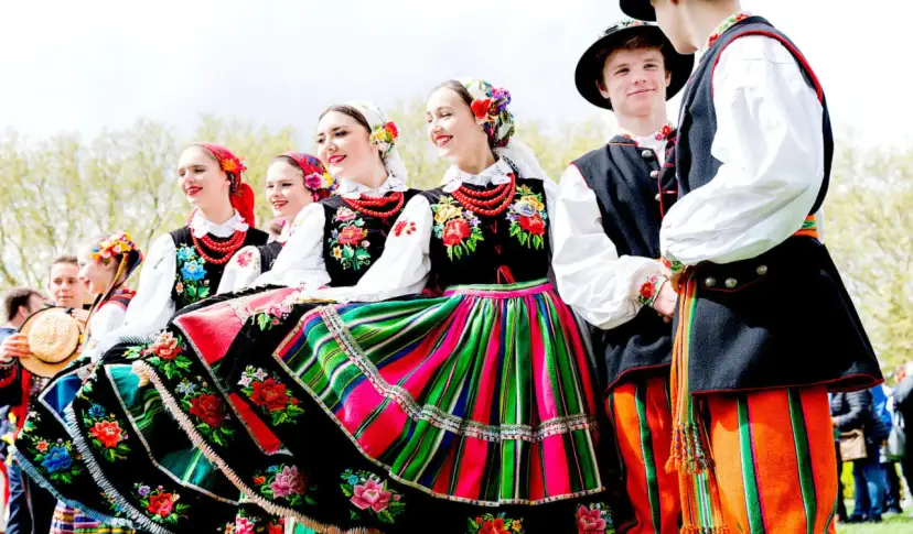 Młodzi ludzie w barwnych strojach ludowych, gotowi do wykonania polskich tańców narodowych.