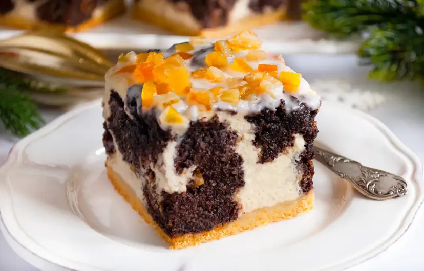 Pyszny sernik z makiem, udekorowany kandyzowaną skórką pomarańczową, na białym talerzyku.