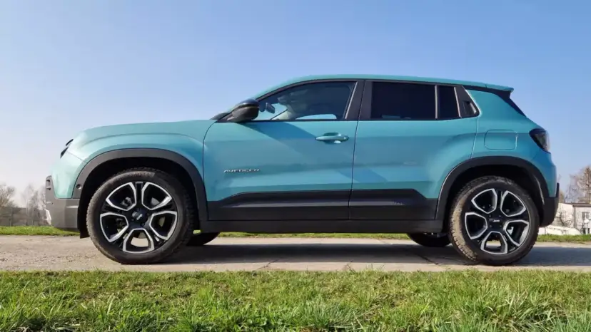 Turkusowy Jeep Avenger 4x4 z czarnymi felgami na tle nieba i trawy.