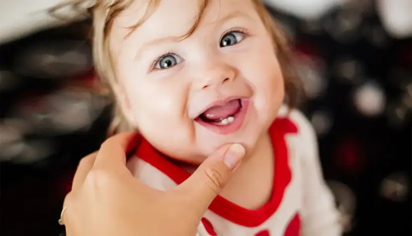 Uśmiechnięte dziecko z widocznymi ząbkami, które właśnie wychodzą. Delikatne dziąsła przy ząbkowaniu są lekko zaczerwienione.
