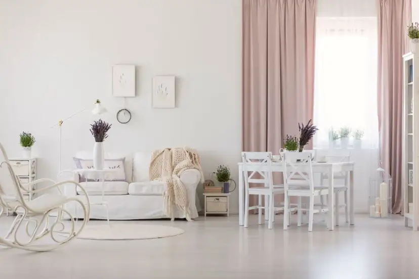 Jasny salon w stylu prowansalskim. Biała kanapa, fotel bujany, stół z krzesłami i lawenda tworzą przytulną atmosferę.