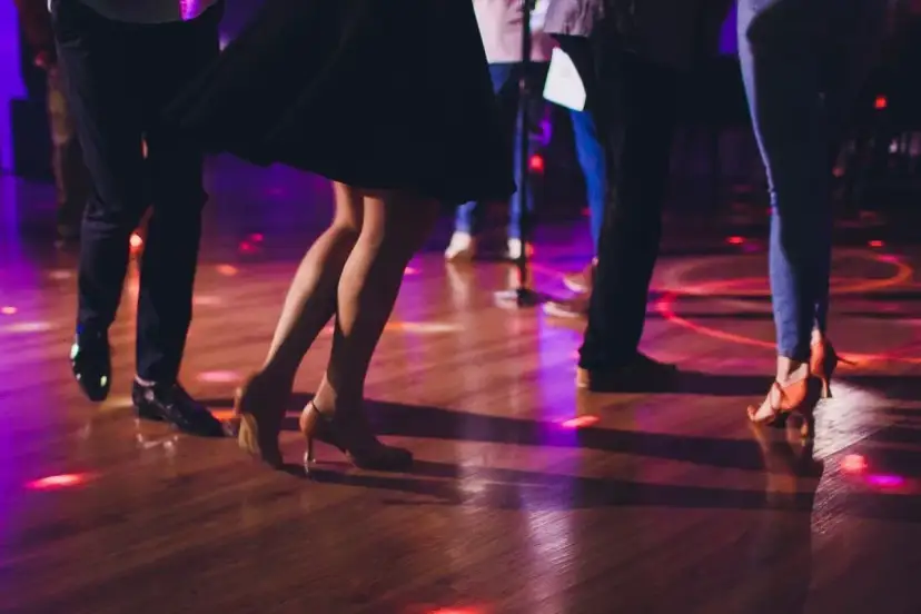 Ludzie tańczą w rytm znanych piosenek, tworząc widowiskowe układy taneczne. Kolorowe światła odbijają się od parkietu.