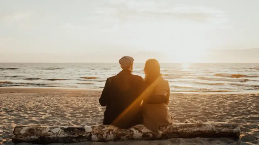 Para dwojga siedząca na pniu na plaży, patrząca na zachód słońca nad morzem. Idealne, fajne miejsce nad morzem dla dwojga.