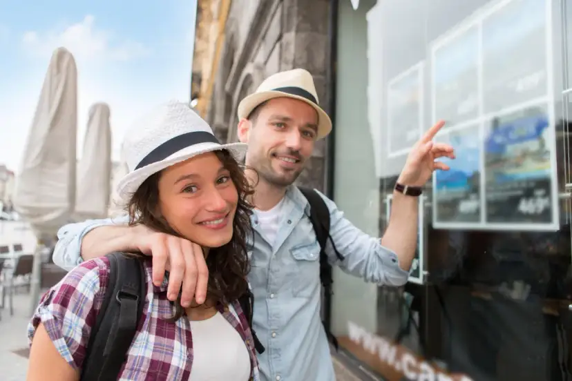 Para uśmiechniętych turystów w kapeluszach patrzy w okno biura podróży.