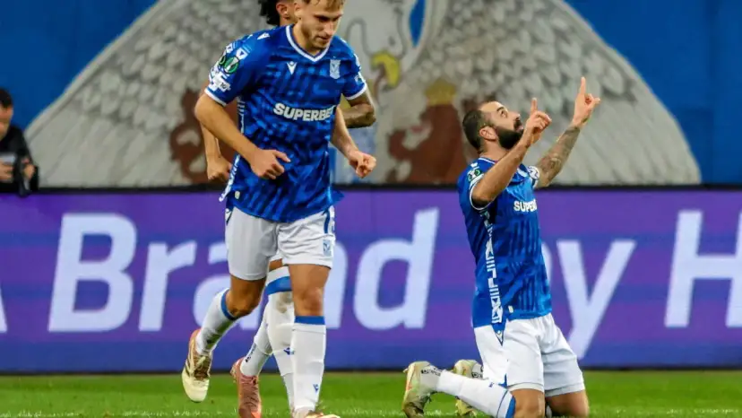 Piłkarz klęczy na boisku, celebrując bramkę. W tle biegnie kolega z drużyny. Wszyscy w niebieskich strojach. Czekamy, kiedy wraca ekstraklasa!