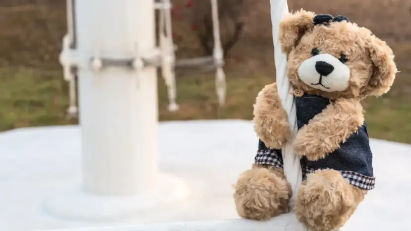 Pluszowy miś w dżinsowej kamizelce siedzi na białej balustradzie.