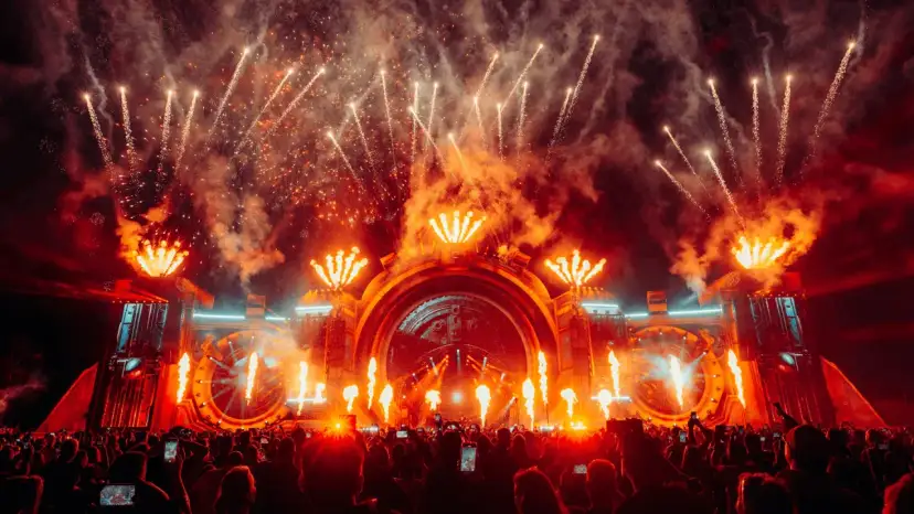 Spektakularny pokaz fajerwerków i płomieni na scenie podczas festiwalu Sunrise Festival 2026. Tłum ludzi z telefonami wzniesionymi ku górze.
