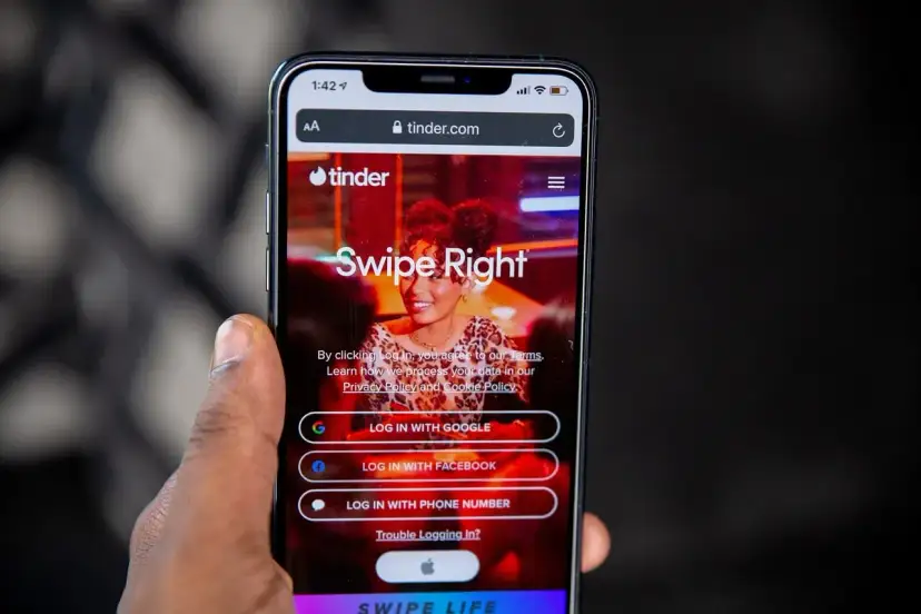 Telefon z aplikacją Tinder. Widoczne opcje logowania: Google, Facebook, numer telefonu. Czas na skróty na Tinderze!