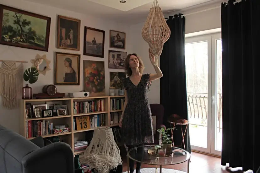 Kobieta w salonie z książkami i obrazami na ścianach, zastanawia się, jak samemu odnowić żyrandol z koralików.