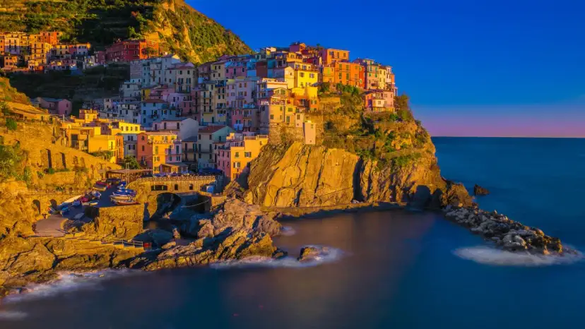 Kolorowe domy Cinque Terre w **Włoszech we wrześniu**, oświetlone złotym słońcem, schodzą ku morzu.