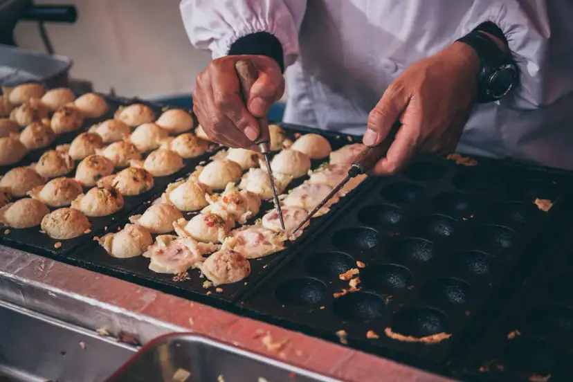 Ręce obracają kulki takoyaki na specjalnej patelni. Ten prosty takoyaki przepis jest w trakcie realizacji.