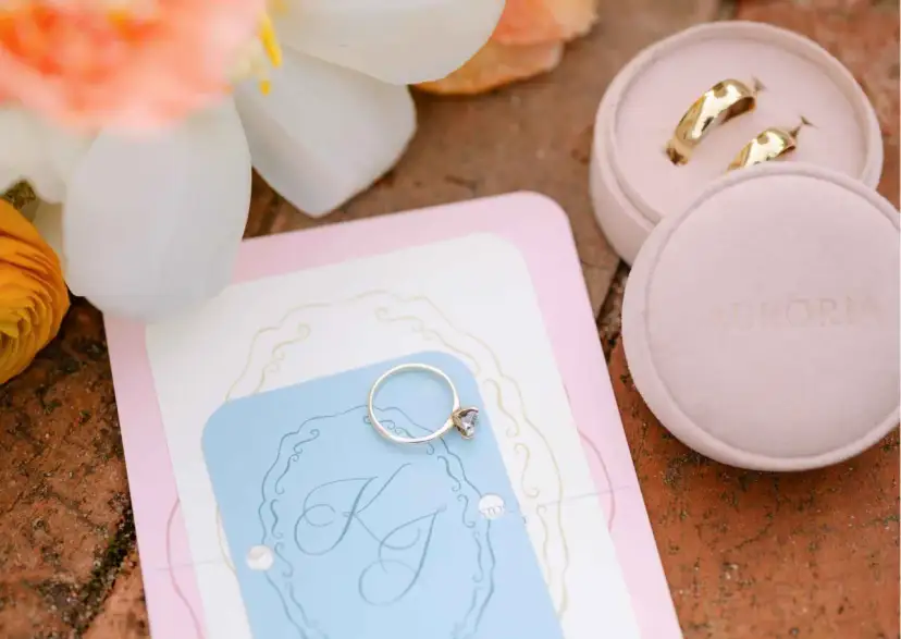 Złote obrączki i pierścionek zaręczynowy na zaproszeniu na randkę. Kwiaty dodają romantyzmu.