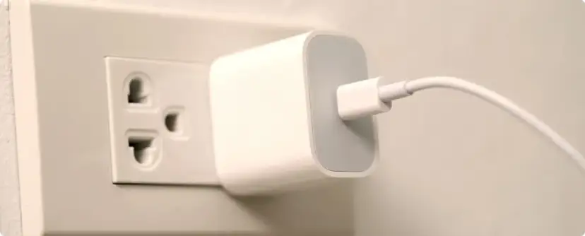 Biała ładowarka z kablem podłączona do gniazdka elektrycznego. Typ wtyczki EU.