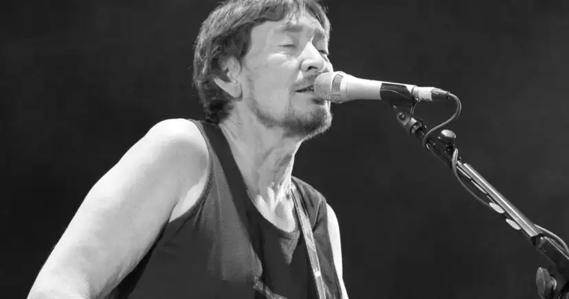 Chris Rea nie żyje. Muzyk śpiewa do mikrofonu na czarnym tle, w czarnej koszulce bez rękawów.