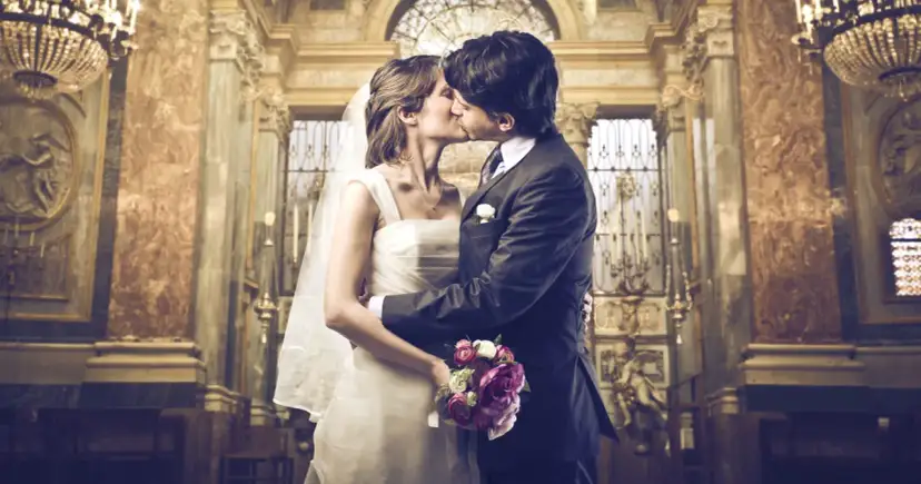 Para młoda całująca się w kościele, panna młoda w bieli, pan młody w garniturze.